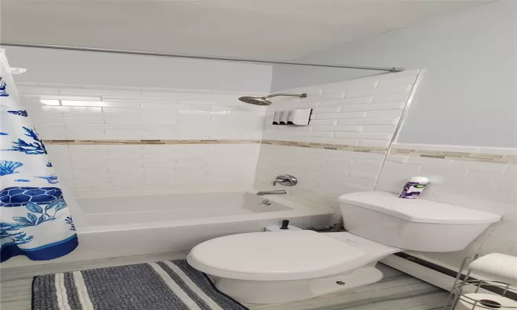 Bathroom featuring shower / bath combo with shower curtain, tile walls, and toilet