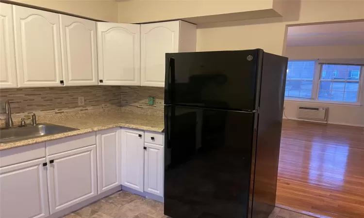 Kitchen with an AC wall unit, white cabinetry, black refrigerator, and sink