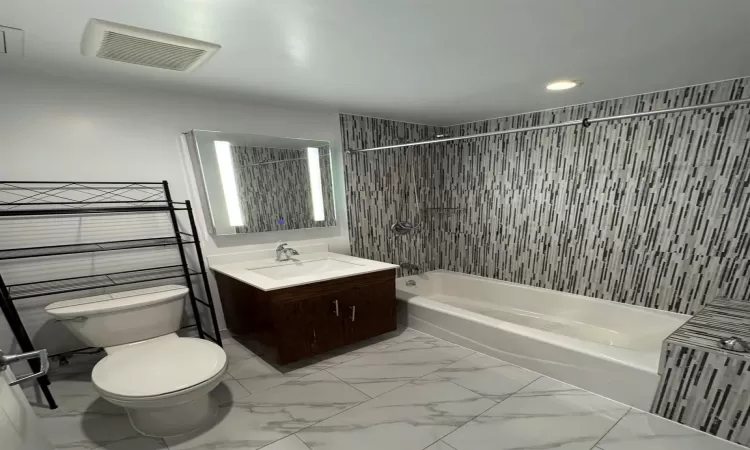 Full bathroom with vanity, tiled shower / bath combo, toilet, and tile walls