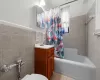 Full bathroom featuring shower / bath combo, tile patterned floors, toilet, vanity, and tile walls