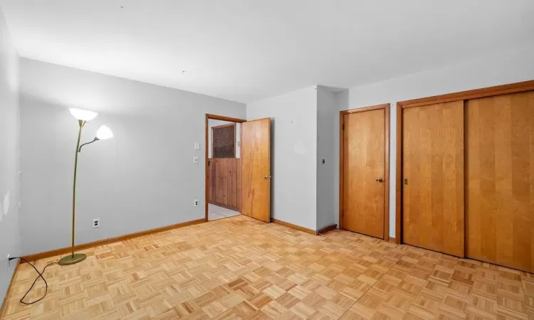 Unfurnished bedroom with multiple closets and light parquet flooring