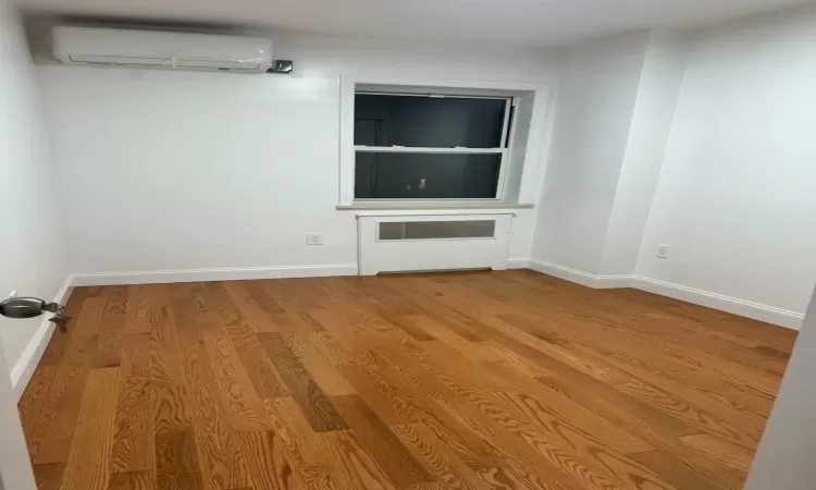 Empty room featuring an AC wall unit and light wood-type flooring