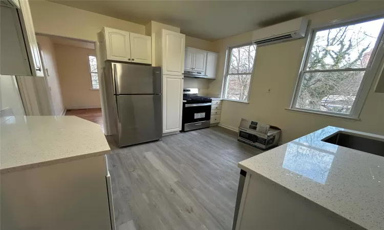 Kitchen with light stone countertops, white cabinetry, stainless steel appliances, an AC wall unit, and light hardwood / wood-style floors