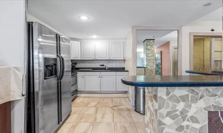 Kitchen featuring stainless steel fridge, backsplash, sink, white cabinets, and range