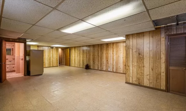 Basement with stainless steel fridge, a drop ceiling, and wooden walls