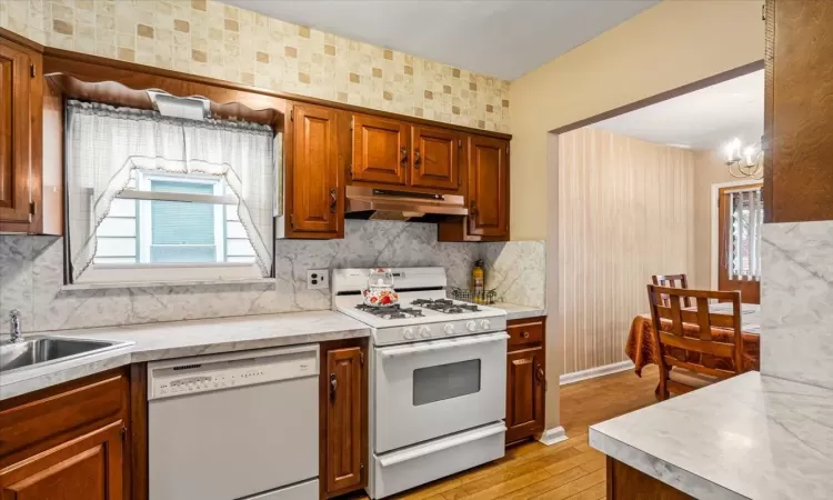 Kitchen featuring sink, light hardwood / wood-style flooring, a chandelier, white appliances, and decorative backsplash