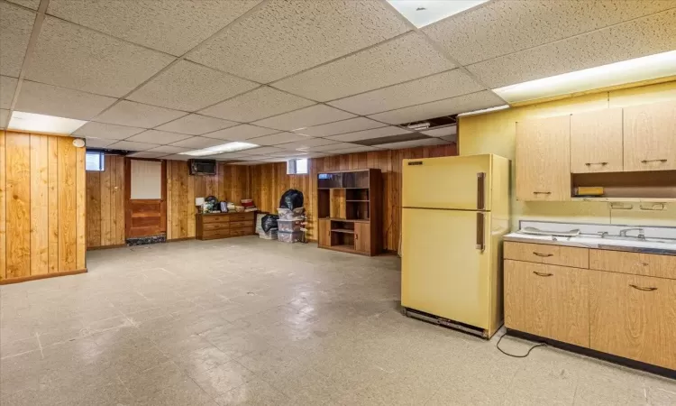 Kitchen with white fridge, a drop ceiling, wooden walls, and sink