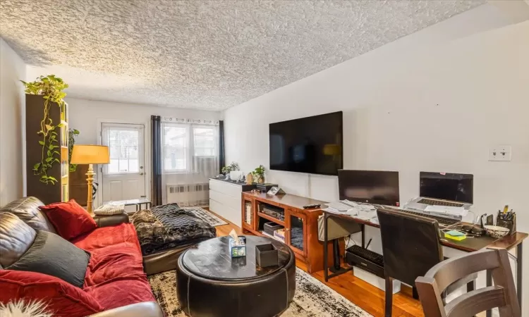 Living room with radiator heating unit, a textured ceiling, hardwood / wood-style flooring, and lofted ceiling