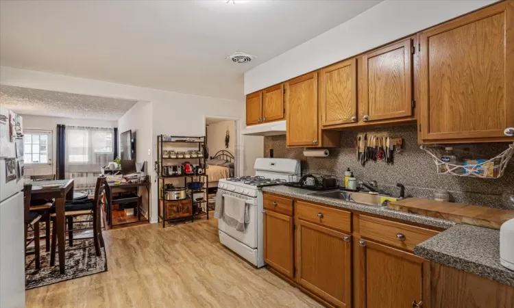 Kitchen featuring sink, light wood-type flooring, a textured ceiling, tasteful backsplash, and white range with gas cooktop