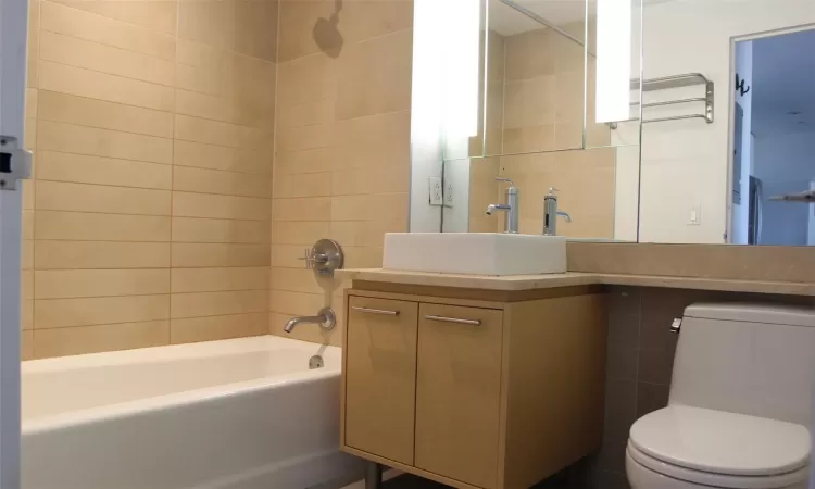 Full bathroom featuring tiled shower / bath, vanity, toilet, and tile walls