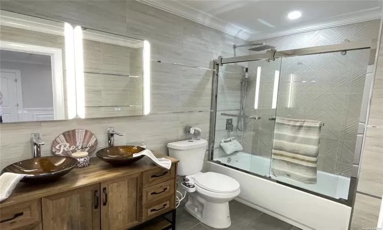 Full bathroom featuring vanity, bath / shower combo with glass door, tile patterned flooring, ornamental molding, and tile walls