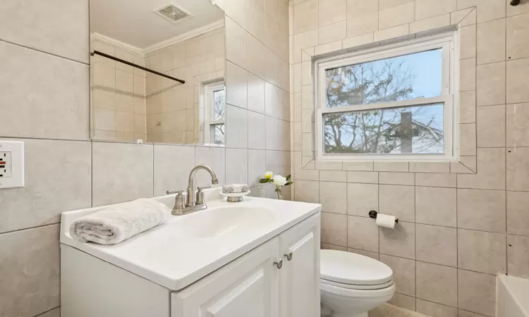 Full bathroom with ornamental molding, vanity, shower / washtub combination, tile walls, and toilet