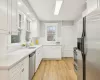 Kitchen with sink, decorative backsplash, light wood-type flooring, white cabinetry, and stainless steel appliances