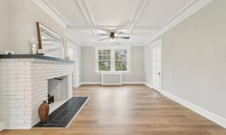 Unfurnished living room with hardwood / wood-style floors, coffered ceiling, ceiling fan, a fireplace, and beamed ceiling