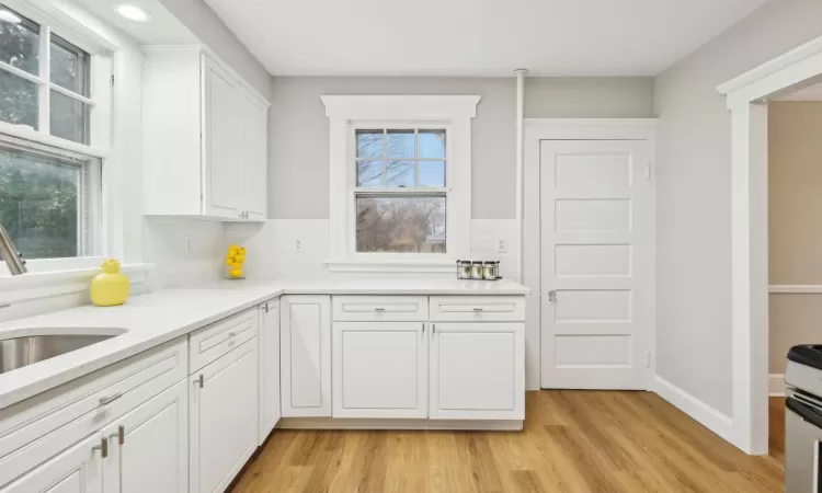 Kitchen with tasteful backsplash, plenty of natural light, white cabinets, and light hardwood / wood-style flooring