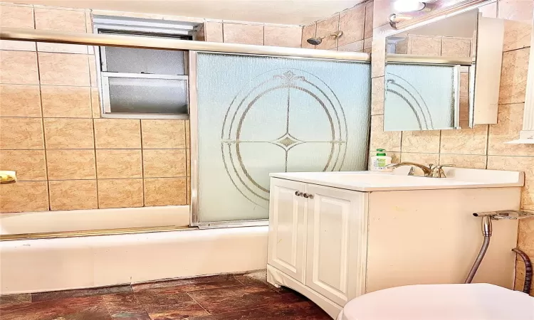 Full bathroom featuring vanity, toilet, tile walls, and bath / shower combo with glass door