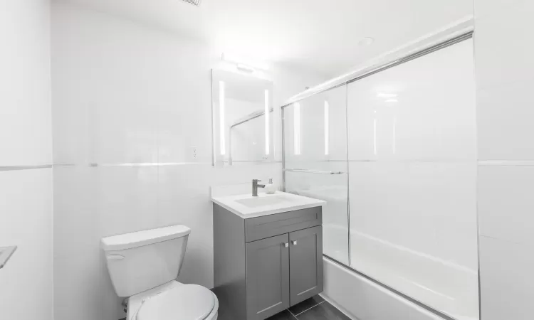 Full bathroom featuring enclosed tub / shower combo, tile patterned floors, toilet, vanity, and tile walls