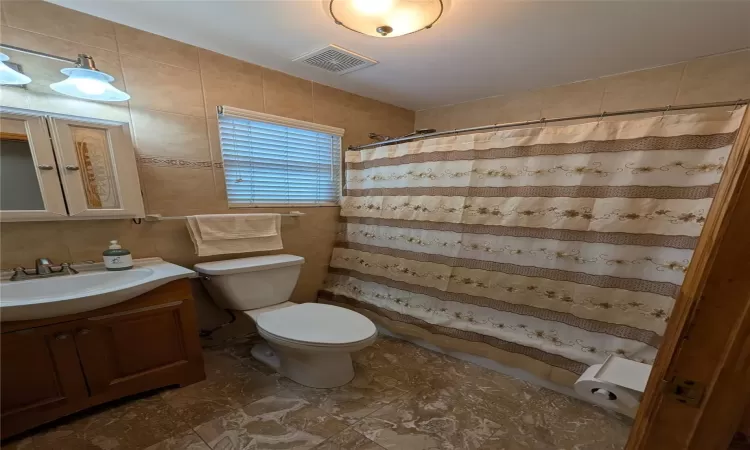 Bathroom with a shower with curtain, vanity, tile walls, and toilet