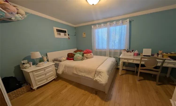 Bedroom featuring a wall mounted air conditioner, ornamental molding, and light hardwood / wood-style flooring