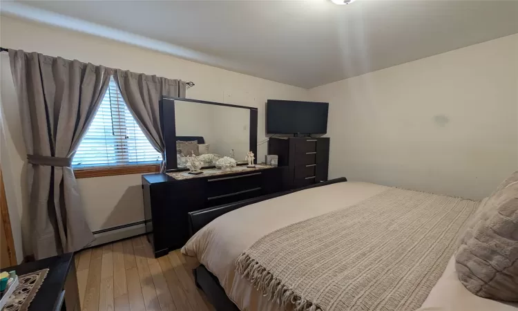 Bedroom with light hardwood / wood-style floors and a baseboard heating unit