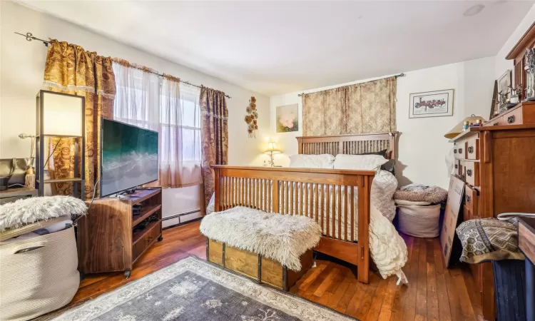 Bedroom with dark wood-type flooring and a baseboard heating unit