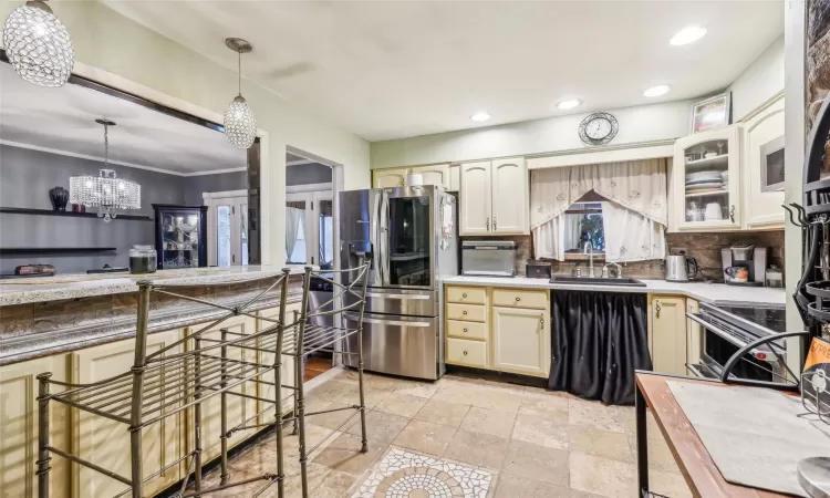 Kitchen featuring sink, hanging light fixtures, a notable chandelier, decorative backsplash, and appliances with stainless steel finishes