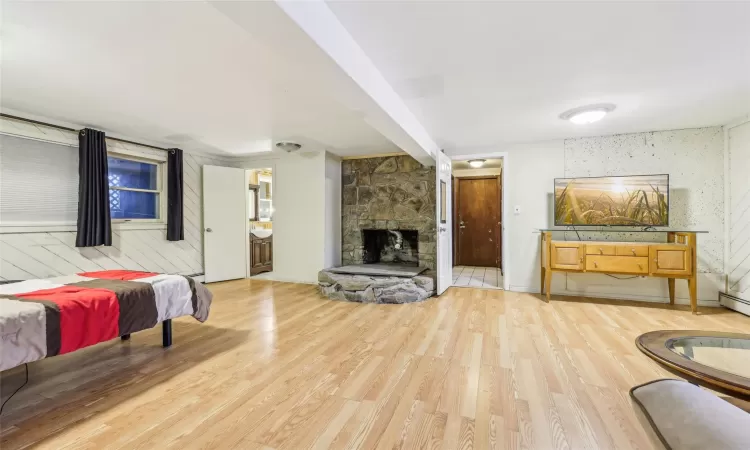 Bedroom featuring a baseboard heating unit, ensuite bathroom, wood-type flooring, wooden walls, and a fireplace