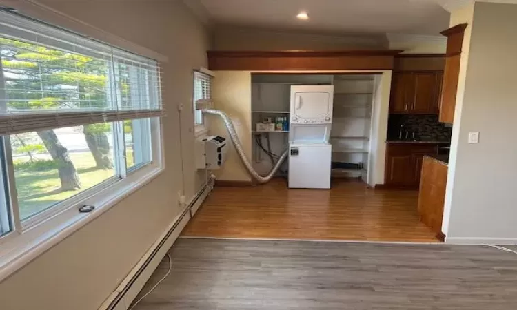 Laundry room with crown molding, a wall mounted air conditioner, wood-type flooring, and stacked washer / drying machine