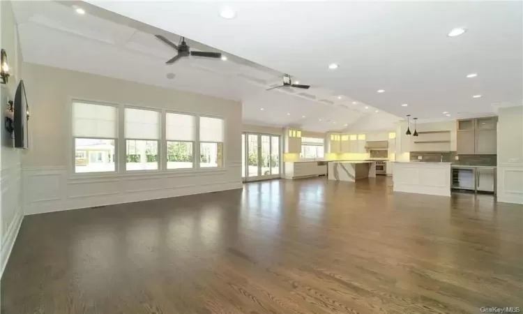 Unfurnished living room with beam ceiling, wine cooler, ceiling fan, and dark hardwood / wood-style flooring. FOR MARKETING PURPOSES ONLY.