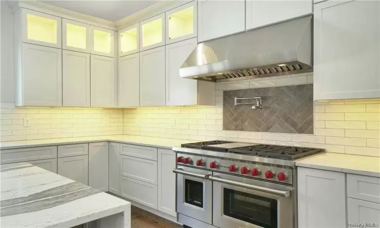 Kitchen with exhaust hood, white cabinets, range with two ovens, tasteful backsplash, and light stone counters. FOR MARKETING PURPOSES ONLY.