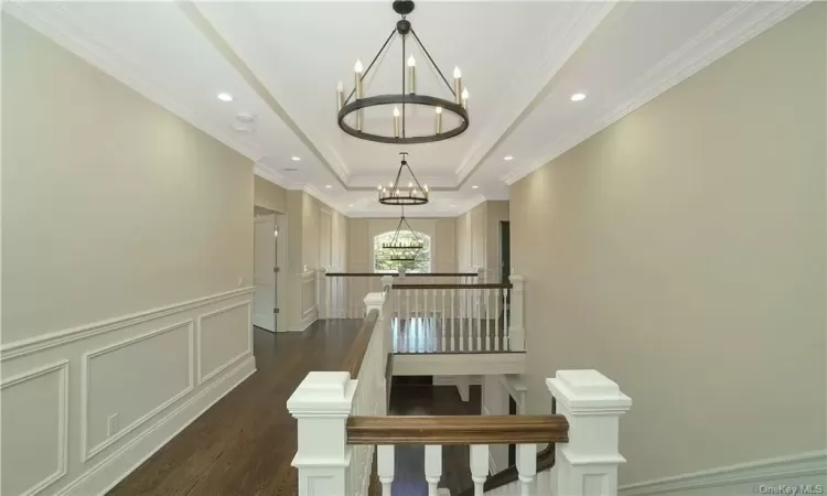 Corridor with a tray ceiling, dark hardwood / wood-style flooring, a chandelier, and ornamental molding. FOR MARKETING PURPOSES ONLY.