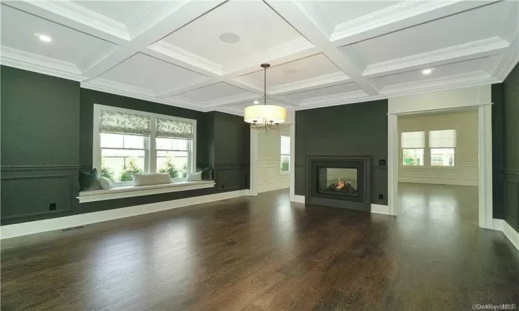 Unfurnished living room with beam ceiling, coffered ceiling, a multi sided fireplace, dark hardwood / wood-style flooring, and ornamental molding. FOR MARKETING PURPOSES ONLY.