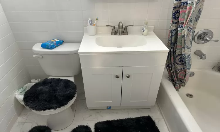 Full bathroom featuring shower / bath combo, vanity, toilet, and tile walls