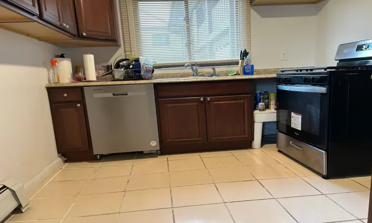 Kitchen with dishwasher, black stove, a baseboard radiator, dark brown cabinets, and light tile patterned flooring