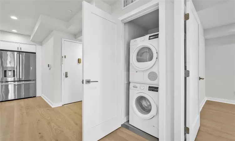 Laundry room with light hardwood / wood-style flooring and stacked washer / drying machine