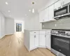 Kitchen with light hardwood / wood-style flooring, tasteful backsplash, decorative light fixtures, white cabinetry, and stainless steel appliances