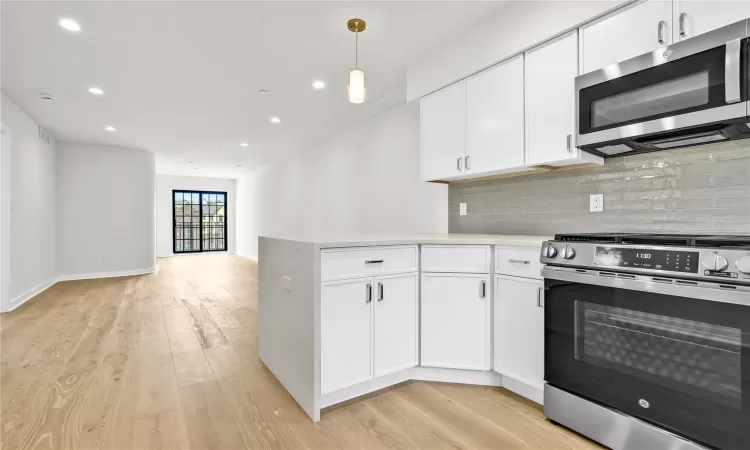 Kitchen with light hardwood / wood-style flooring, tasteful backsplash, decorative light fixtures, white cabinetry, and stainless steel appliances