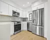 Kitchen with decorative backsplash, light wood-type flooring, white cabinetry, and appliances with stainless steel finishes