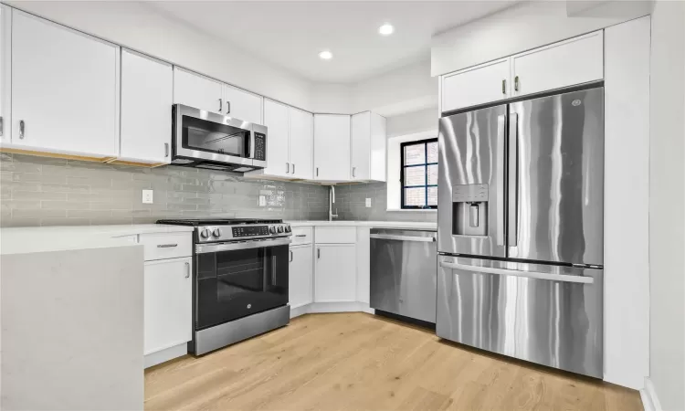 Kitchen with decorative backsplash, light wood-type flooring, white cabinetry, and appliances with stainless steel finishes