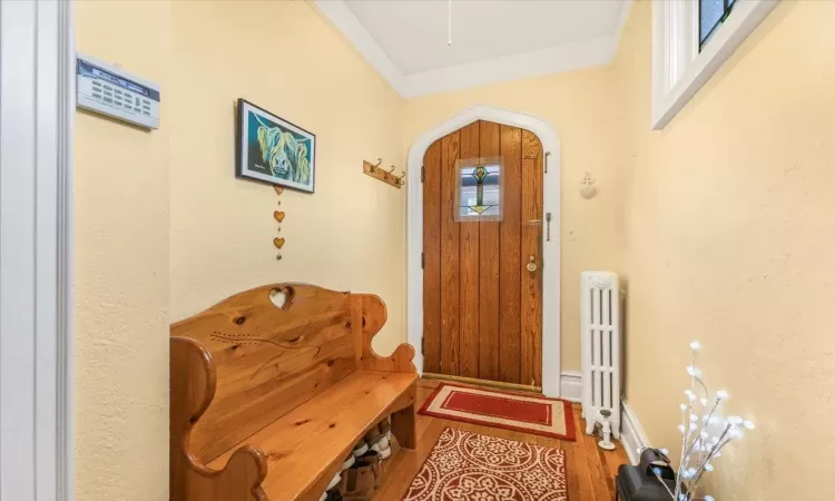 Entrance foyer featuring wood-type flooring, radiator heating unit, and ornamental molding