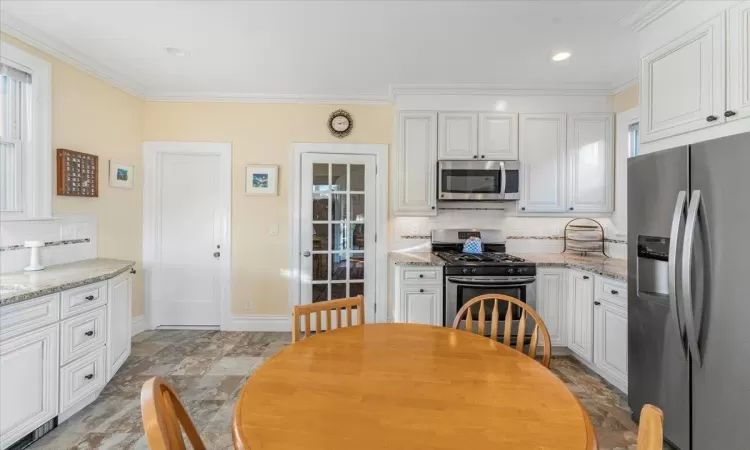 Kitchen featuring white cabinets, appliances with stainless steel finishes, tasteful backsplash, and light stone counters