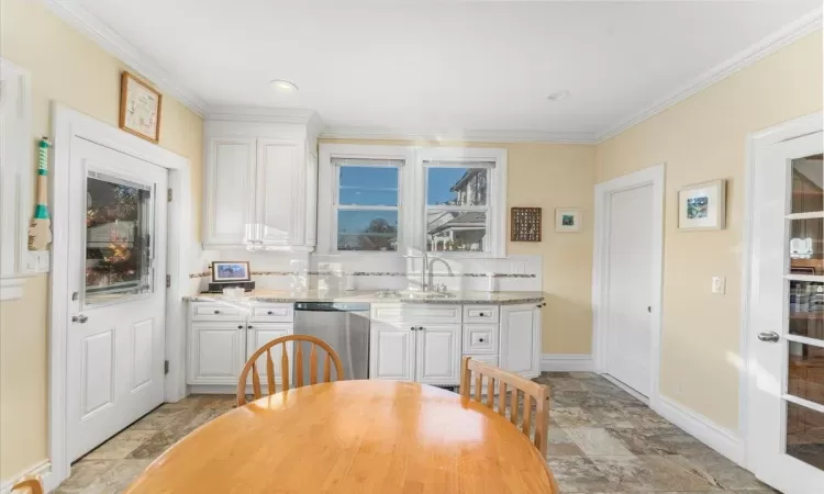 Kitchen with light stone countertops, dishwasher, sink, tasteful backsplash, and white cabinets