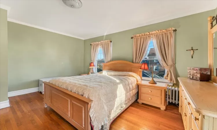 Bedroom with multiple windows, radiator heating unit, wood-type flooring, and ornamental molding