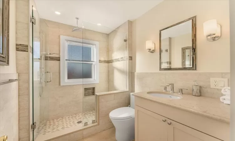 Bathroom featuring vanity, a shower with shower door, and tile walls