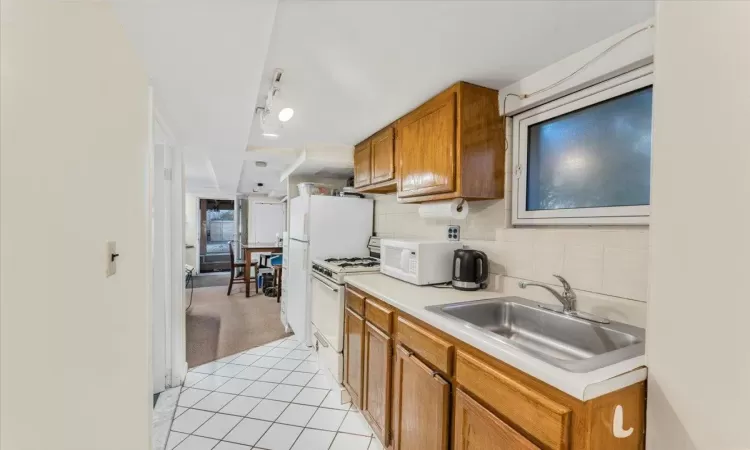 Kitchen with sink, white appliances, backsplash, and light tile patterned floors