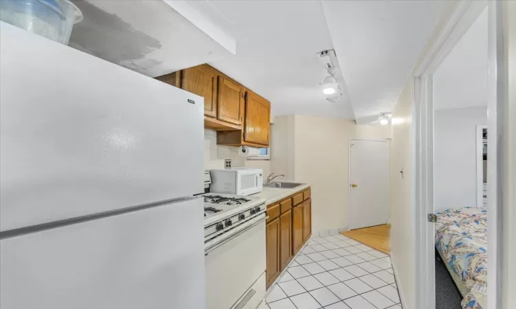 Kitchen with white appliances, backsplash, track lighting, sink, and light tile patterned floors