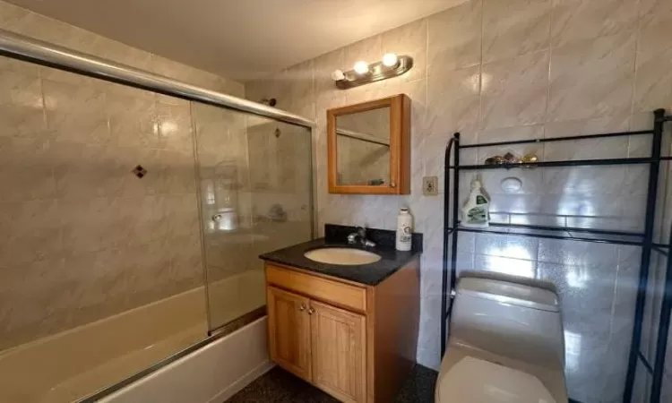 Full bathroom with vanity, toilet, enclosed tub / shower combo, and tile walls