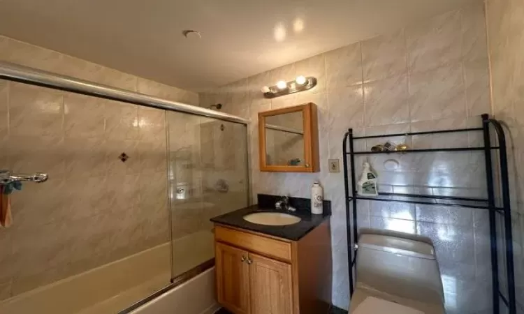 Full bathroom featuring toilet, vanity, tile walls, and combined bath / shower with glass door