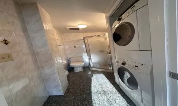 Clothes washing area featuring stacked washer / dryer and tile walls