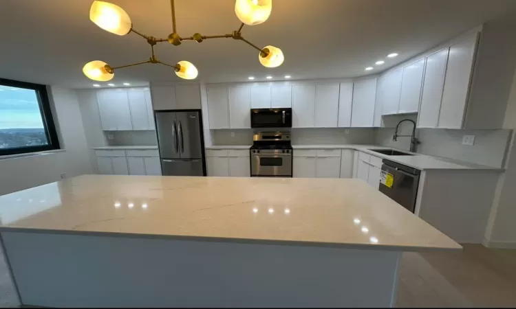 Kitchen featuring light stone countertops, sink, stainless steel appliances, pendant lighting, and white cabinets